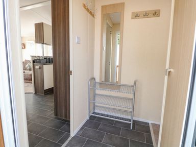 An entryway with a wall mirror shoe rack and coat hooks leading to a kitchen and living area at Audrey's Lodge Foxburrow Hang in Fritton