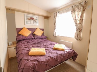 A bedroom with a double bed with purple bedding and two yellow towels on the bed at Audrey's Lodge Foxburrow Hang in Fritton