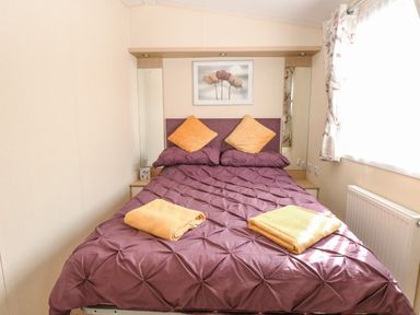 A bedroom with a double bed with purple bedding and two yellow pillows with folded yellow towels on the bed at Audrey's Lodge Foxburrow Hang in Fritton