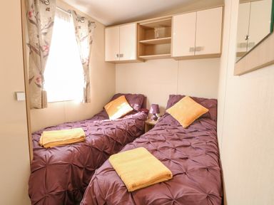 A bedroom with two single beds with purple bedding and yellow towels and pillows at Audrey's Lodge Foxburrow Hang in Fritton