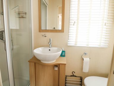 A bathroom with a sink on a wooden cabinet a shower toilet paper holder and a window with blinds at Audrey's Lodge Foxburrow Hang in Fritton