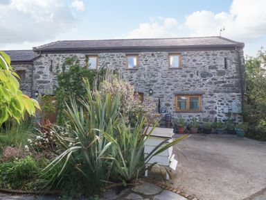 A stone house with multiple windows and a garden with plants and a white beehive in front at Ty Gwennol in Llanddona near Beaumaris