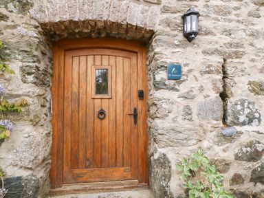 A wooden door set in a stone wall with a small window a door knocker and a wall lamp at Ty Gwennol in Llanddona near Beaumaris