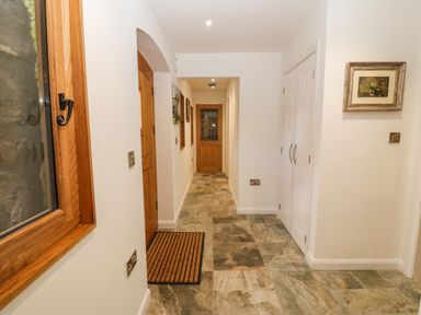 A hallway with stone tile flooring wooden doors a window with wooden frame and white walls at Ty Gwennol in Llanddona near Beaumaris