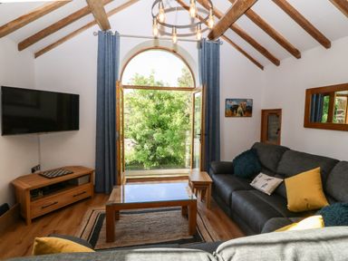 A living room with a large arched window gray sofas and a wooden coffee table at Ty Gwennol in Llanddona near Beaumaris