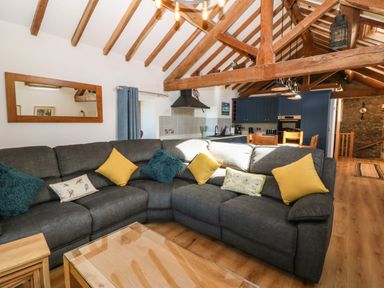 A spacious living room with a gray sectional sofa with colorful cushions and an open kitchen with blue cabinets at Ty Gwennol in Llanddona near Beaumaris