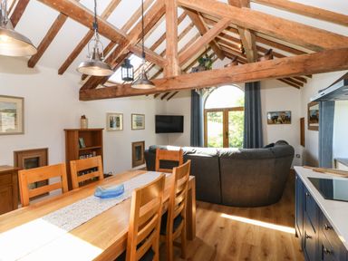 A living and dining area with wooden dining table and chairs grey sofa blue kitchen cabinets and exposed wooden beams at Ty Gwennol in Llanddona near Beaumaris