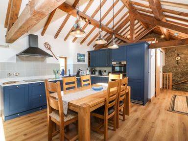 A kitchen with blue cabinets wooden dining table and chairs under exposed wooden beams at Ty Gwennol in Llanddona near Beaumaris