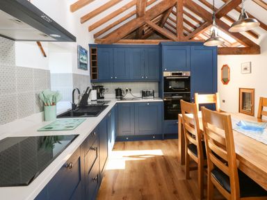 A kitchen with blue cabinets wooden beams and a dining table with chairs at Ty Gwennol in Llanddona near Beaumaris