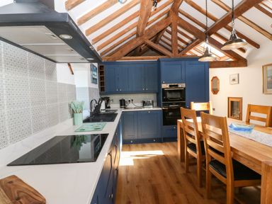 A kitchen with blue cabinets wooden ceiling beams a dining table and chairs at Ty Gwennol in Llanddona near Beaumaris