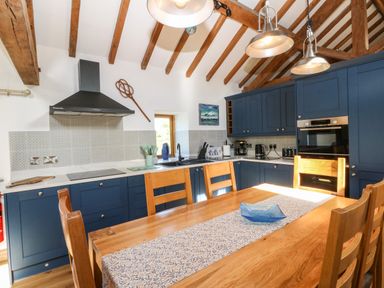 A kitchen with blue cabinets wooden dining table and chairs under exposed wooden beams at Ty Gwennol in Llanddona near Beaumaris