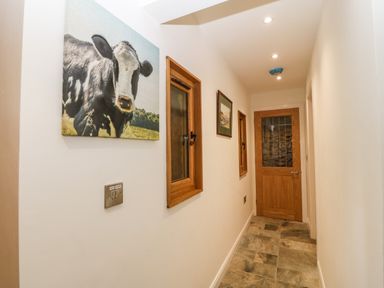 A hallway with stone tile floor wooden door and framed pictures on walls at Ty Gwennol in Llanddona near Beaumaris