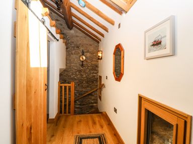 A hallway with wooden floor and beams stone wall and a wooden sliding door at Ty Gwennol in Llanddona near Beaumaris