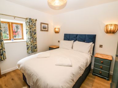 A bedroom with a blue headboard bed two bedside tables with lamps and floral curtains at Ty Gwennol in Llanddona near Beaumaris