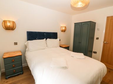A bedroom with a double bed two bedside tables a wardrobe and wooden door at Ty Gwennol in Llanddona near Beaumaris