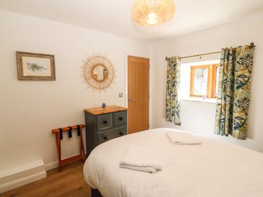A bedroom with a bed and white linens a wooden dresser a round mirror and patterned curtains at Ty Gwennol in Llanddona near Beaumaris