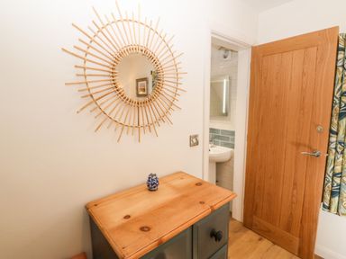 A wooden cabinet with a small blue decorative item and a round rattan mirror on the wall near a wooden door leading to a bathroom at Ty Gwennol in Llanddona near Beaumaris