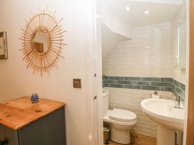 A small bathroom with a toilet and sink next to a wooden cabinet with a decorative mirror on the wall at Ty Gwennol in Llanddona near Beaumaris