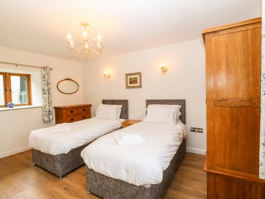A bedroom with two single beds wooden dresser wardrobe and a window at Ty Gwennol in Llanddona near Beaumaris