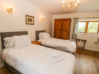 A bedroom with two single beds a wooden wardrobe and a window at Ty Gwennol in Llanddona near Beaumaris