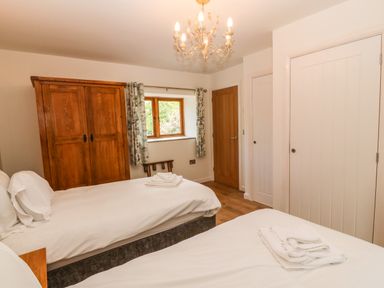 A bedroom with two beds wooden wardrobe window with curtains and two doors at Ty Gwennol in Llanddona near Beaumaris