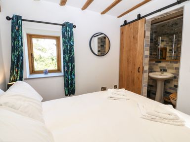 A bedroom with a bed towels window with curtains and a door leading to a bathroom at Ty Gwennol in Llanddona near Beaumaris