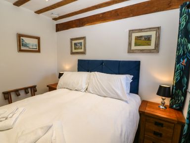 A bedroom with a double bed wooden bedside tables lamps and framed pictures on the walls at Ty Gwennol in Llanddona near Beaumaris
