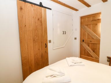 A bedroom corner with wooden barn doors a white cupboard and folded towels on a bed at Ty Gwennol in Llanddona near Beaumaris