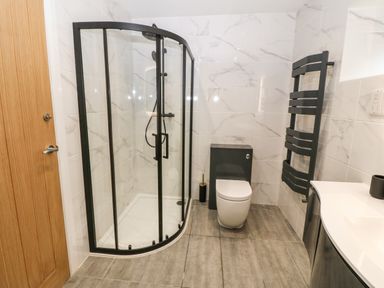 A bathroom with a curved glass shower enclosure a toilet a heated towel rail and a sink at Ty Gwennol in Llanddona near Beaumaris