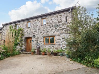 A stone house facade with wooden door and windows with plants in pots and greenery around at Ty Gwennol in Llanddona near Beaumaris