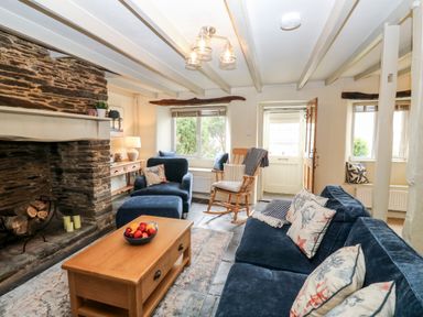A living room with a stone fireplace wooden coffee table blue furniture and a rocking chair at Alexanders Cottage in Frogmore