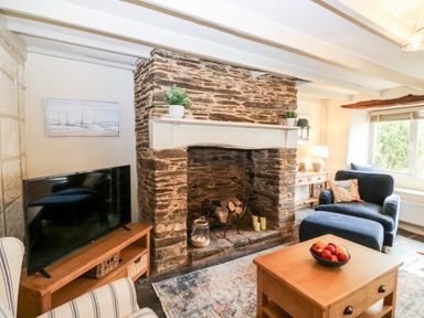 A living room with a stone fireplace a television on a wooden stand and seating at Alexanders Cottage in Frogmore