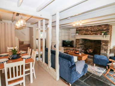 A dining area with a wooden table set for four and a living room with blue couches and a stone fireplace at Alexanders Cottage in Frogmore