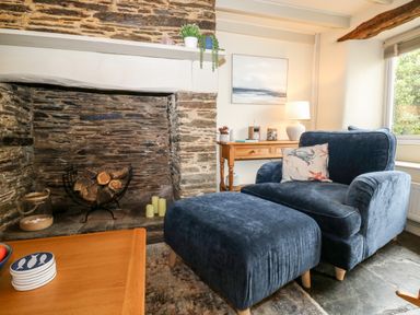 A living room with a stone fireplace a blue armchair and ottoman and a wooden table at Alexanders Cottage in Frogmore