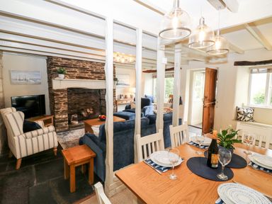 A dining area with set table and a living room with fireplace and sofas at Alexanders Cottage in Frogmore