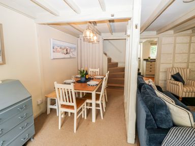 A dining area with a wooden table and white chairs next to a living space with a blue sofa and a striped armchair at Alexanders Cottage in Frogmore