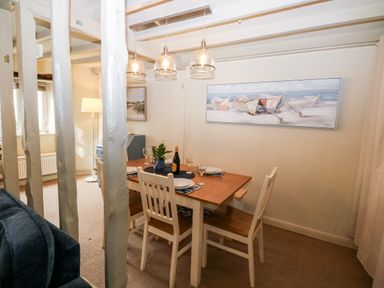 A dining room with a wooden table and four chairs under hanging lights at Alexanders Cottage in Frogmore