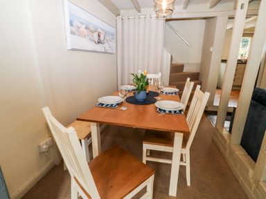 A dining area with a wooden table set for four and chairs near stairs at Alexanders Cottage in Frogmore