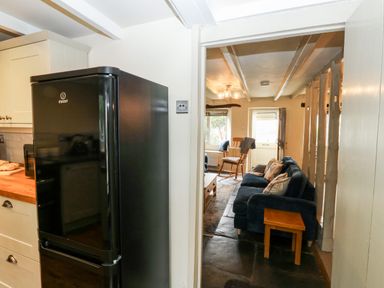 A kitchen with a black refrigerator leading to a living room with a blue sofa and wooden rocking chair at Alexanders Cottage in Frogmore