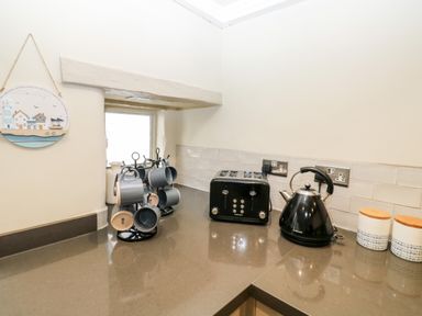 A kitchen countertop with a mug tree holding blue mugs a black toaster a black kettle and two canisters at Alexanders Cottage in Frogmore