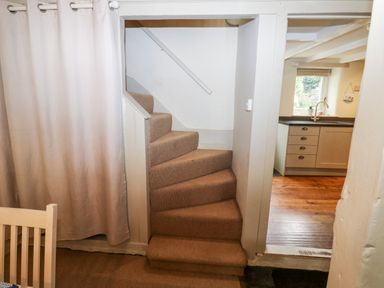 A small staircase with carpet leading up next to a kitchen with wooden floor and cabinets at Alexanders Cottage in Frogmore