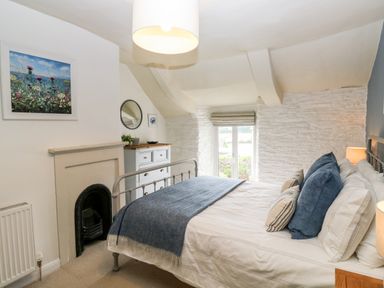 A bedroom with a bed a chest of drawers a window and a small fireplace at Alexanders Cottage in Frogmore