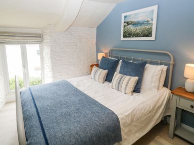 A bedroom with a bed covered with blue and white bedding beside a window and bedside tables with lamps at Alexanders Cottage in Frogmore