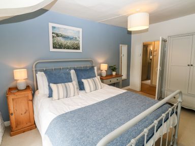 A bedroom with a metal bed frame with blue and white bedding two bedside tables with lamps a wardrobe and a wall painting at Alexanders Cottage in Frogmore