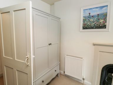 A room corner with a closed white wardrobe a white door a white radiator and a framed floral painting above at Alexanders Cottage in Frogmore