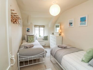 A bedroom with two single beds a white dresser a window and a hanging lamp at Alexanders Cottage in Frogmore