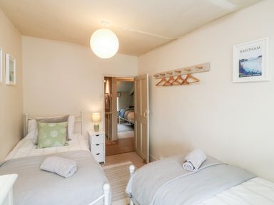 A bedroom with two single beds a bedside table with a lamp and a wall rack with hangers at Alexanders Cottage in Frogmore