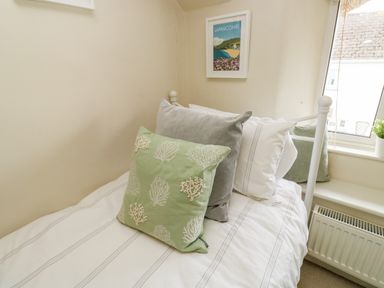 A small bed with multiple pillows next to a window and radiator at Alexanders Cottage in Frogmore