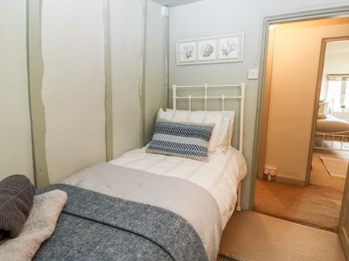 A bedroom with a single bed and patterned pillow next to a doorway with a view into another bedroom at Alexanders Cottage in Frogmore