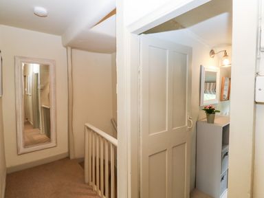 A hallway with a wall mirror and a door leading to a room with a cabinet and a small potted plant at Alexanders Cottage in Frogmore